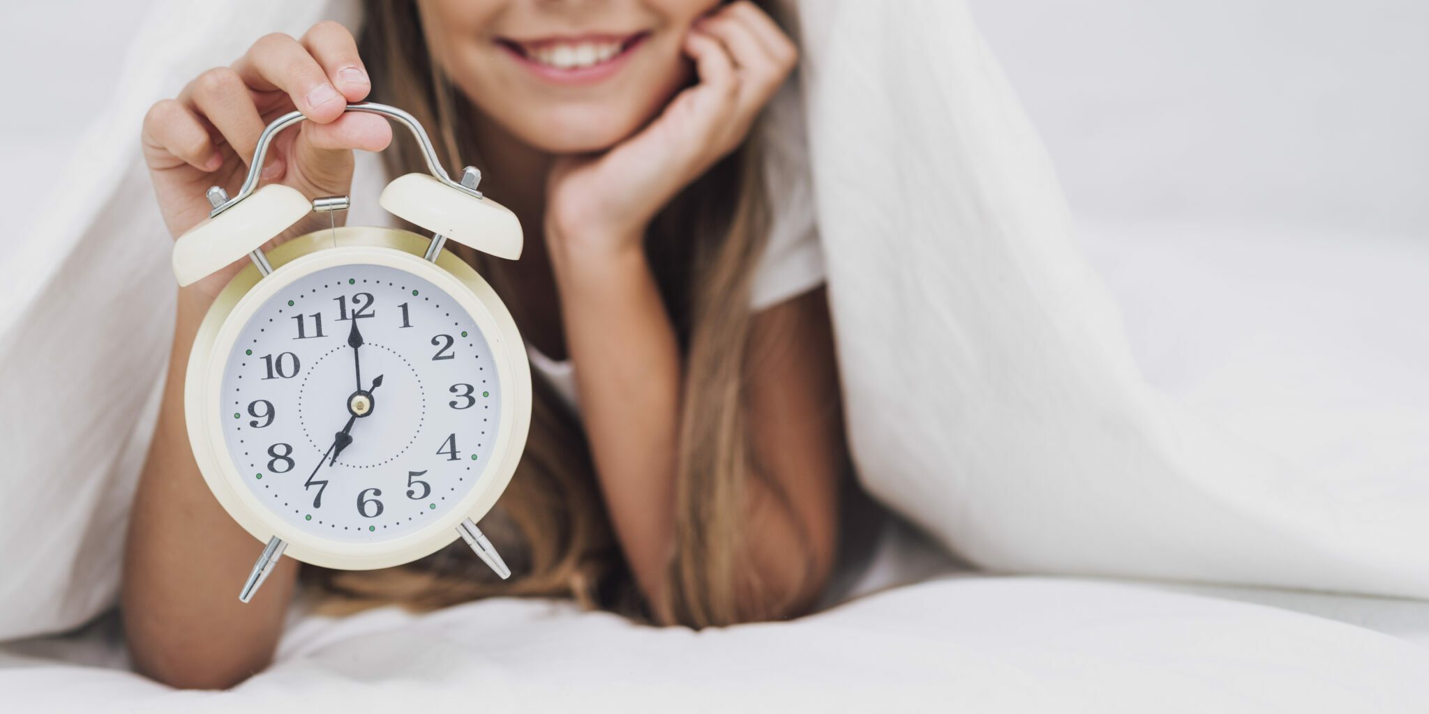 Ritmo-circadiano immagine di una ragazza sotto le coperte con in mano una sveglia